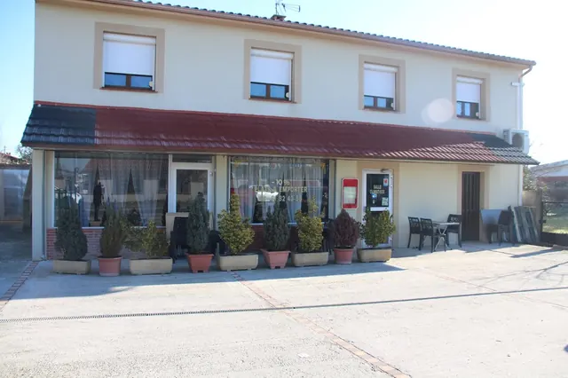 La façade du restaurant, son auvent rouge et ses plantes, avec le parking devant